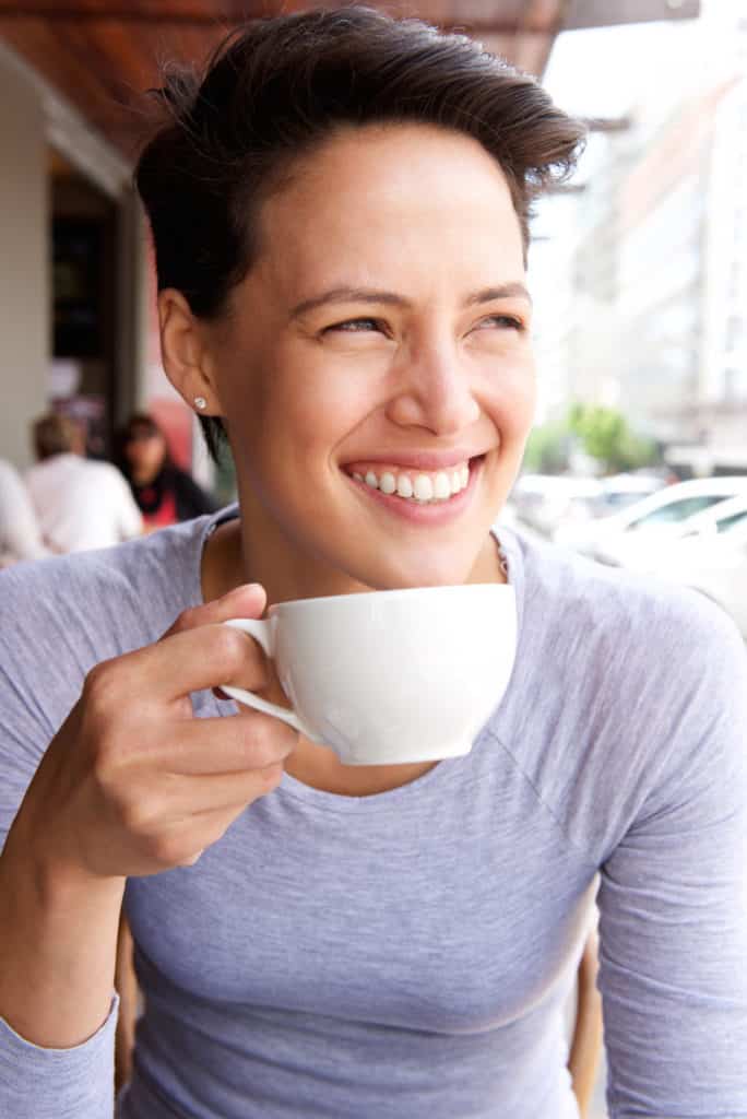 Smiling young woman drinking cup of coffee at cafe